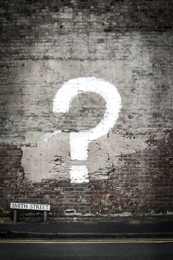 A white question mark painted on a faded brick wall.